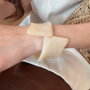 Detalle de un brazalete de resina crema retorcido en la muñeca con ropa de lino