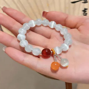 Dettaglio di un elegante bracciale in pietra occhio di gatto bianco con ciondoli colorati
