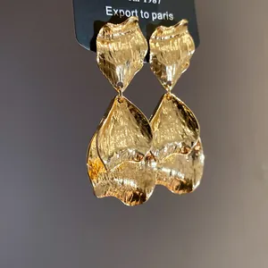 Macro detail of gold metal earrings featuring an artistic wrinkled petal design for women