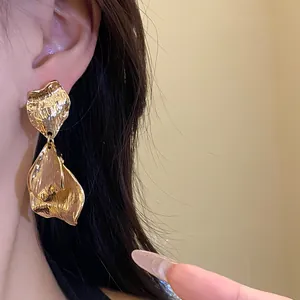 Detailed close-up showing textured gold wrinkled petal drop earrings worn on a model's ear