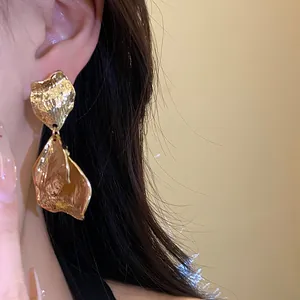 Macro detail of elegant gold-toned metal pleated petal earrings worn on a model's ear