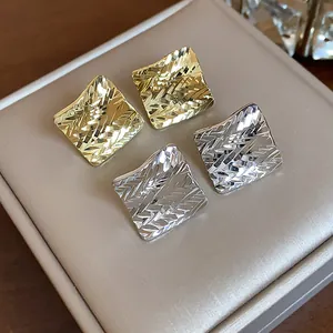 Close-up of gold and silver rhombus stud earrings with a stylish textured finish