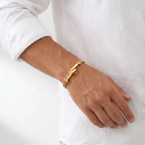 Detailopname van een herenarmband van goud gevlochten roestvrij staal met nagelsluiting.