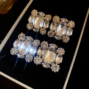 Detaillierte Nahaufnahme von funkelnden quadratischen Strass-Ohrclips in einer schwarzen Box
