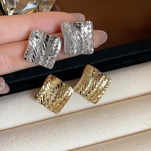 Close-up of minimalist textured rhombus stud earrings in gold and silver finish