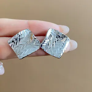 Macro detail showing the geometric diamond-patterned texture on silver stud earrings