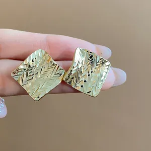 Detailed macro view of gold-tone rhombus stud earrings with intricate textured geometric pattern.