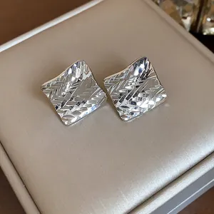 Close-up of silver rhombus stud earrings with elegant geometric diamond-cut pattern texture.