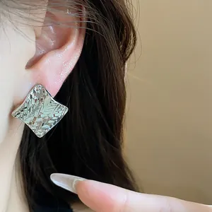 Detailed close-up of minimalist silver rhombus earrings with elegant textured surface