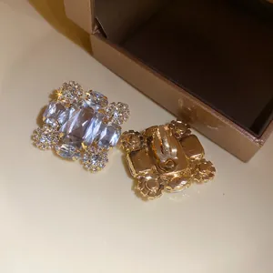 Detailansicht von goldfarbenen Clip-Ohrringen mit eckigen Kristallen und Strasssteinen.
