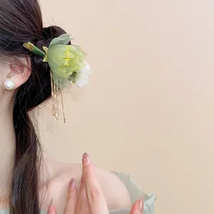Elegant green fabric flower hair clip with gold tassels worn on Asian model's bun