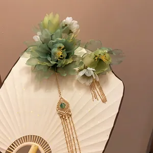 Close-up of teal fabric flower hair clip with golden tassels on a traditional fan