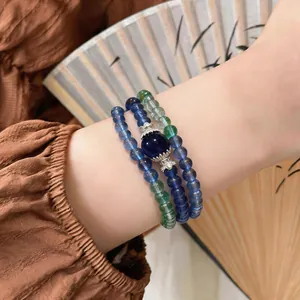 Close-up view of layered blue and green stone beaded bracelets on wrist with folding fan