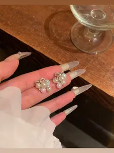 Detailed view of elegant bowknot stud earrings with colorful pearls held on fingers