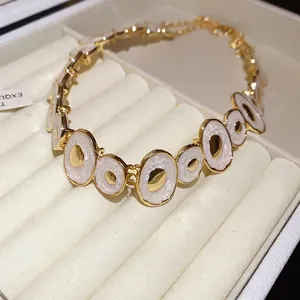 Vintage irregular gold-plated necklace featuring white enamel oval pendants on a jewelry tray