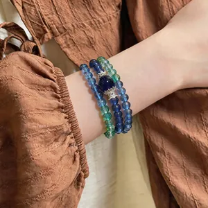 Stacked beaded bracelets with blue and green stone beads on a wrist in a vintage aesthetic
