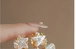 Close-up of pink mother-of-pearl star earrings with gold accents and crystal details.