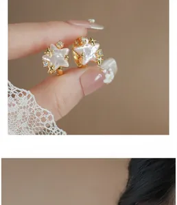 Close-up detail of pink shell star hoop earrings with gold stars and zircon.
