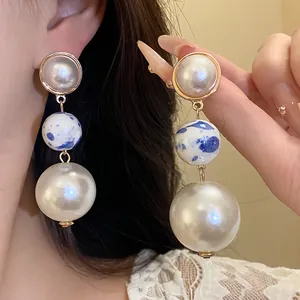 Close-up of elegant drop earrings with large pearls and blue and white ceramic beads.