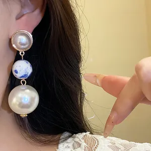 Detailed macro shot of vintage style ceramic and pearl triple bead drop earrings on a model