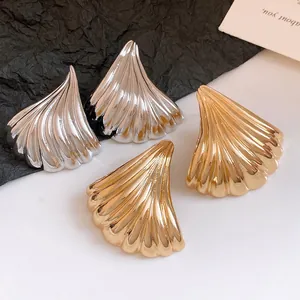 Dettaglio di orecchini a ventaglio in metallo oro e argento con texture a pieghe.