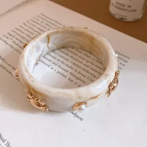 Close-up of a marbled resin bangle featuring detailed gold-tone crab motifs and pearls