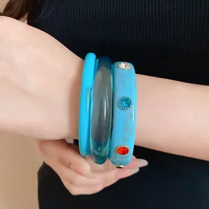 Close-up detail of three stylish resin bangles in blue shades with colorful gemstone accents