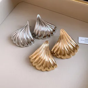 Dettaglio ravvicinato di orecchini a ventaglio in metallo in finiture oro e argento.
