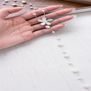 Close-up of a long pearl beaded necklace with a shimmering zircon flower pendant