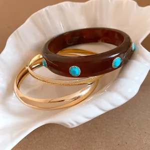 Detail of retro resin and gold bangles set in a white shell dish for a bohemian summer look.