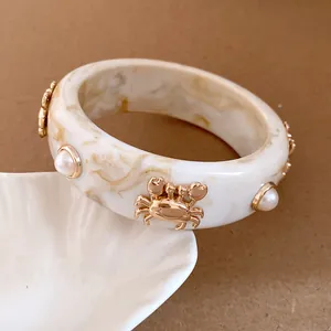 Detailed macro view of a vintage marble resin bangle with gold crab charms and pearls