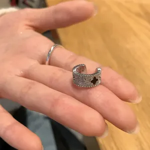 Close-up of a silver-toned ear cuff with quatrefoil cutouts shown on a person's hand.
