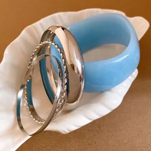 Detailed macro view of bohemian blue resin bangle and textured silver metal bracelets in a dish