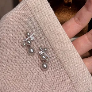 Dettaglio macro di eleganti orecchini a lobo con perle e zirconi su maglia rosa cipria