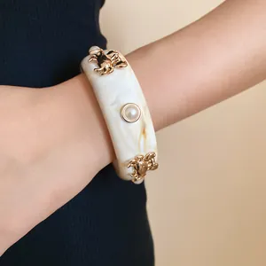 Elegant white resin bangle featuring gold crab charms and pearl details on wrist