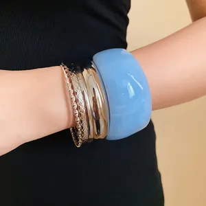 Detail view of a light blue resin bangle paired with metallic textured bracelets on a wrist.