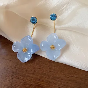 Elegant 18k gold-plated resin flower stud earrings with vibrant blue crystal accents.