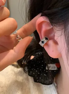 Silver ear cuff featuring black four-leaf clover motifs shown on a model's ear in detail