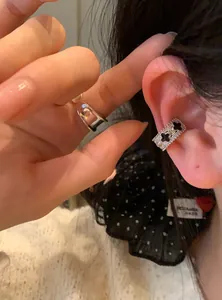 Close-up showing a sparkling silver ear cuff with black clover cutouts on a model's ear