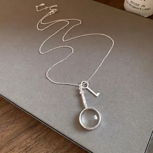 Elegant vintage silver magnifying glass and key charm necklace on a minimalist chain