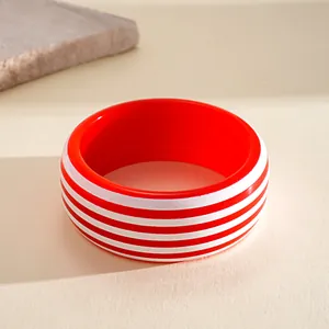 Primer plano de un brazalete de resina a rayas rojas y blancas sobre fondo texturizado