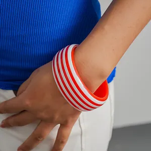 Primer plano de un brazalete de resina a rayas rojas y blancas en la muñeca para moda viva.
