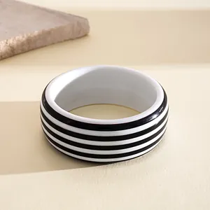 Primer plano de un brazalete de resina a rayas blancas y negras en un fondo neutro