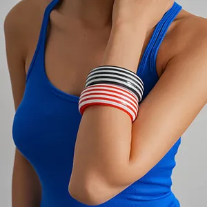 Detalle de brazaletes geométricos de resina a rayas rojas y negras en el brazo de la modelo
