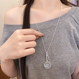 Detailed close-up of a silver circular magnifying glass pendant necklace on a model