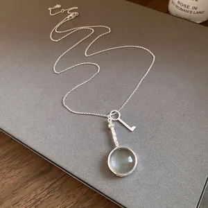 Detailed view of a vintage silver necklace featuring a unique magnifying glass and key pendant.