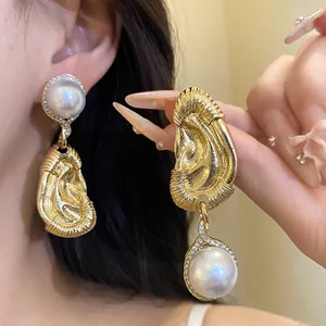 Nahaufnahme von goldenen Vintage-Ohrhängern mit Faltenmetall und großen weißen Perlen