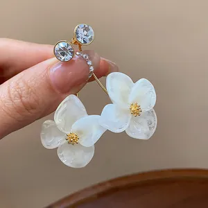 Close-up of elegant 18k gold plated earrings with white resin flower and crystals