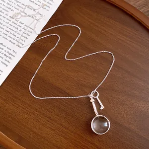 Detailed macro view of vintage silver necklace with magnifying glass and tiny key pendants