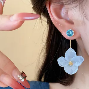 Close-up detail of white resin flower earring with blue crystal stud on model's ear